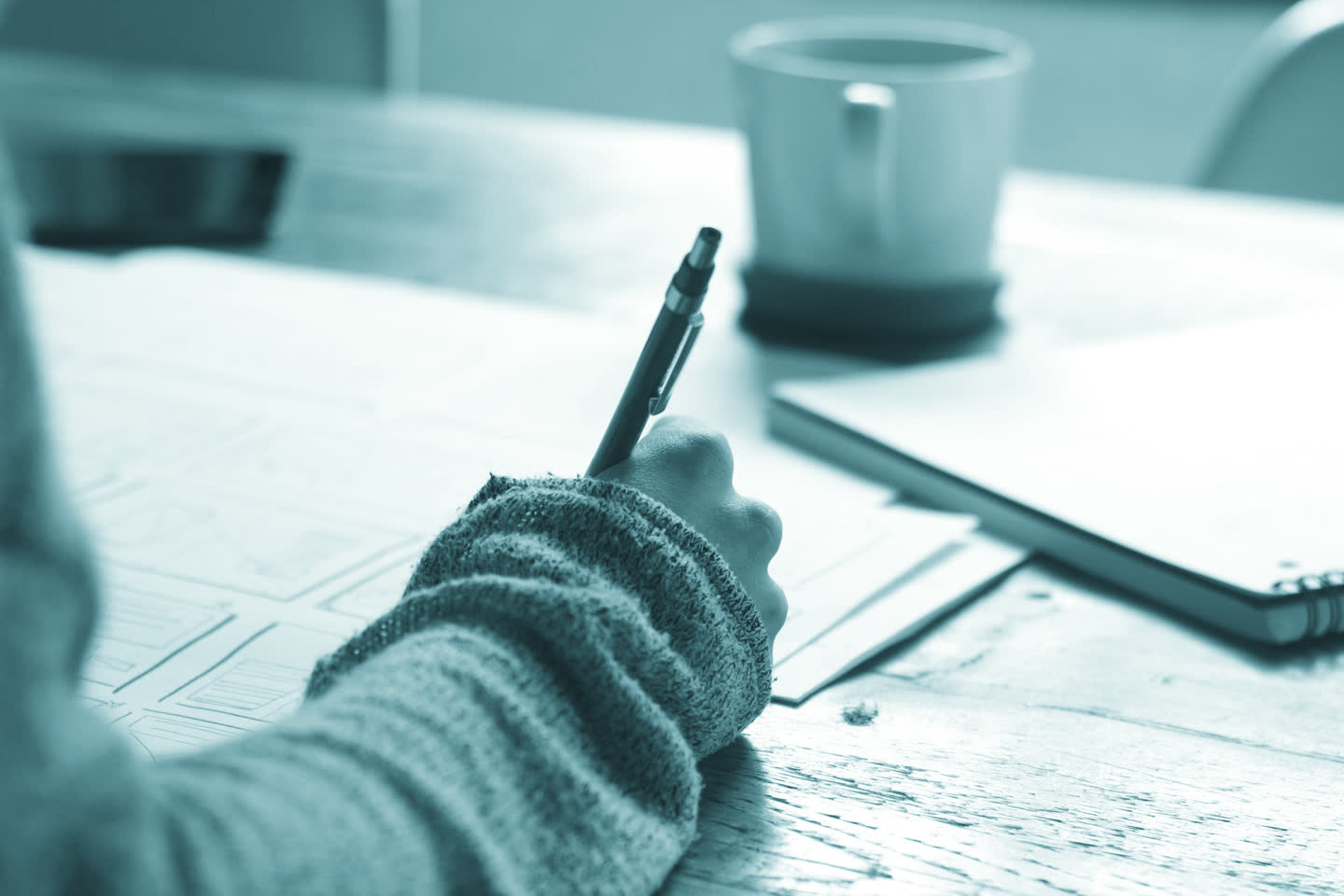 A hand making notes at a working desk