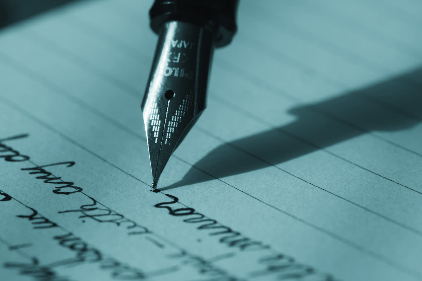 A fountain pen nib writing a line across ruled paper